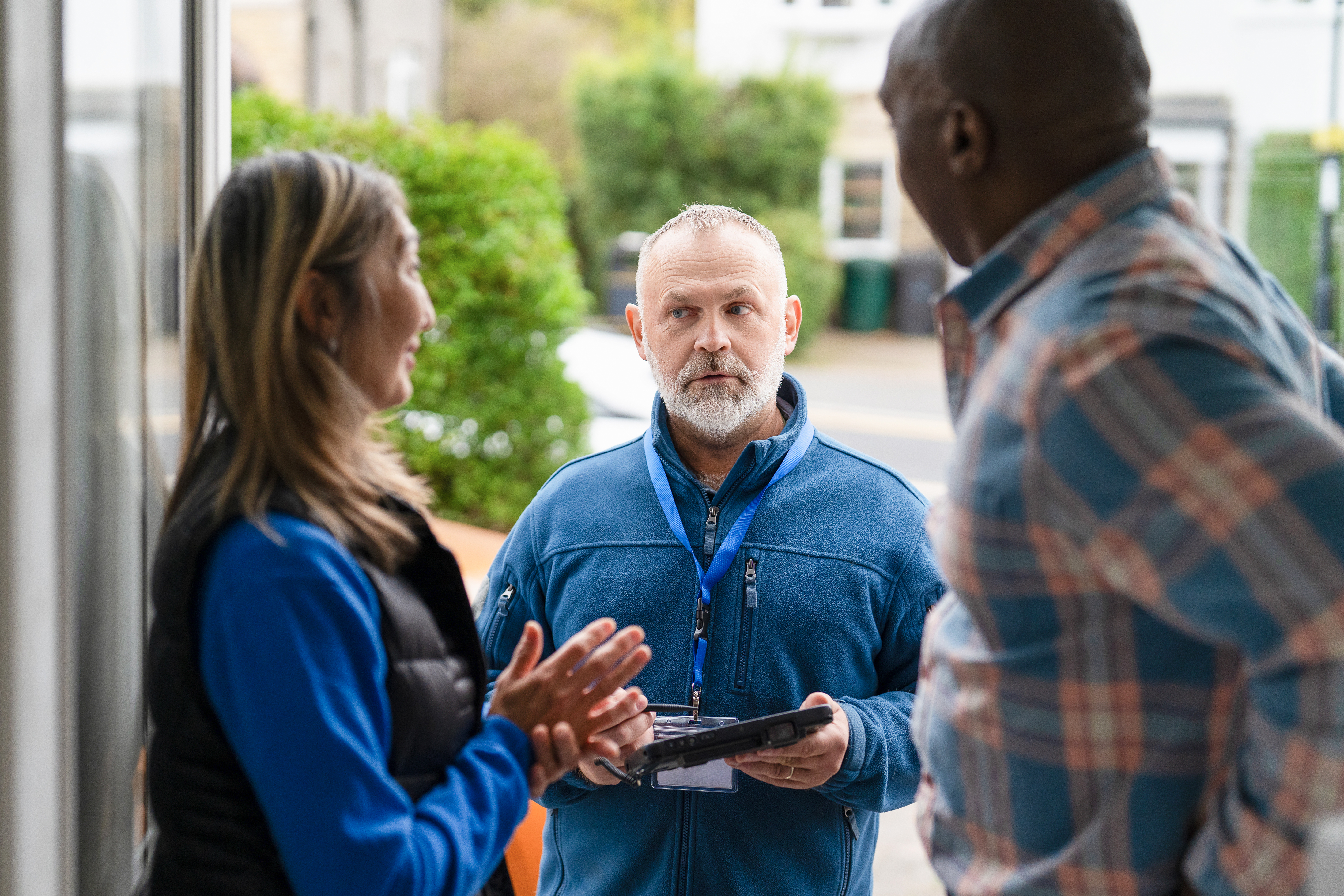 Two community members discuss with a service provider outside a building on a sunny day, sharing ideas and solutions for local needs in their neighborhood.